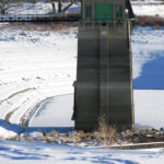 Photo of a reservoir in winter with low water level covered in snow and a water tower coming out of the reservoir
