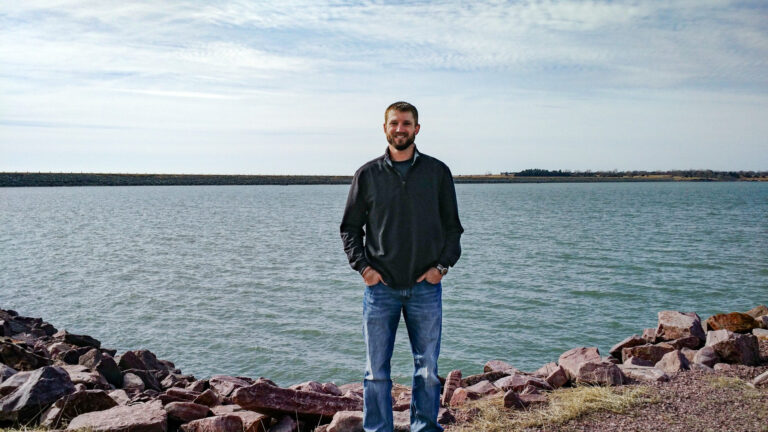 Photo portrait of Matt Lukasiewicz standing in front of a lake