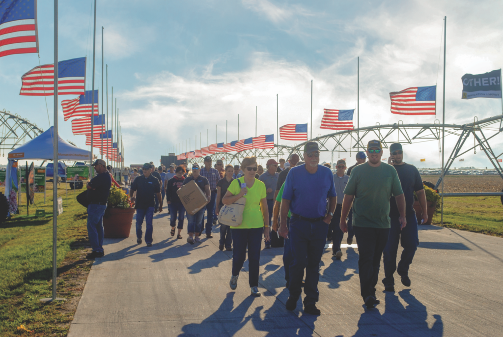 Photo of a crowd of people walking along a road lined with American flags