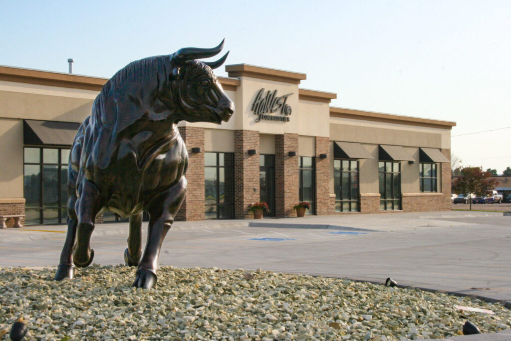 Photo of a bronze bull statue with AgWest main office in the background